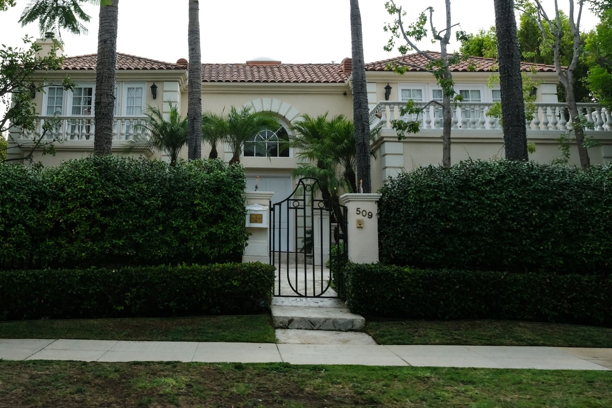 A gated house behind clipped hedges and palms